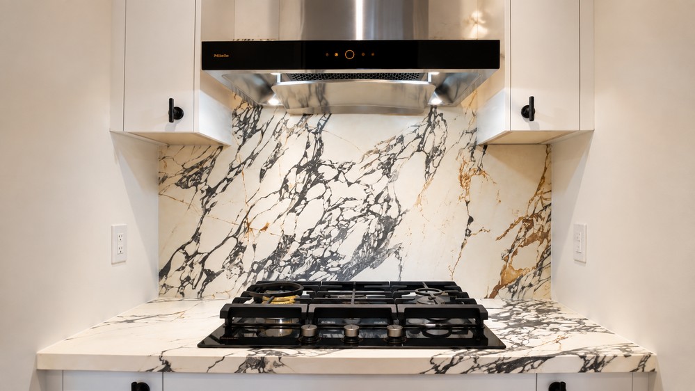 Secondary kitchen gas cooktop with marble backsplash and wall-mount hood